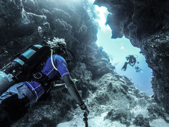 Low angle view of people scuba diving underwater by rock formation