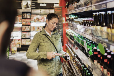 Woman using bar code reader on beer bottle at supermarket