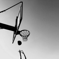 Low angle view of cropped hands playing basketball against clear sky