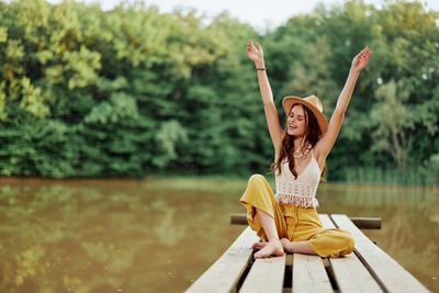 Young woman with arms raised standing against lake