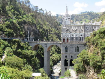 Arch bridge amidst trees and buildings against sky