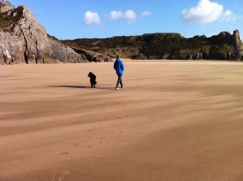 Rear view of man walking with dog on sand