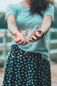 Midsection of woman holding illuminated fairy lights while standing outdoors