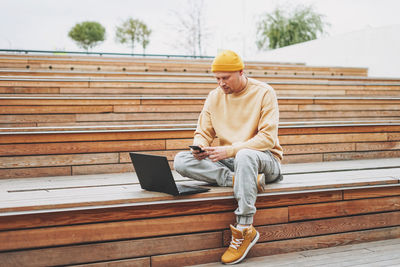 Full length of man using smart phone while sitting on steps outdoors