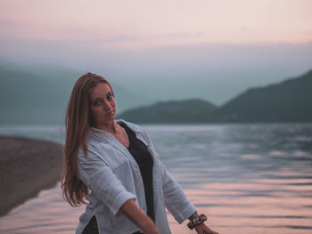 Portrait of young woman standing in sea against sky during sunset