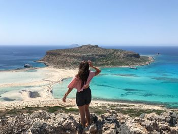 Rear view of woman standing on rocks against clear sky at beach