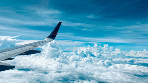 Aerial view of airplane flying over clouds against blue sky