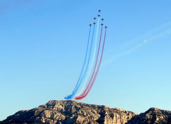 Low angle view of airshow over mountain against blue sky