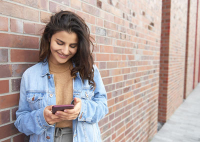 Smiling young man using mobile phone against wall
