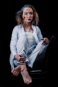 Full length of woman sitting against black background