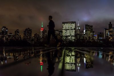 Side view of man jogging on wet footpath with reflection against illuminated skyline