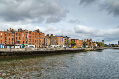 Buildings by river against cloudy sky