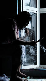 Side view of man looking through window at home