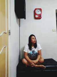 Portrait of young woman sitting against wall