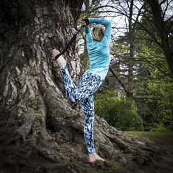 Low angle view of man standing on tree trunk in forest