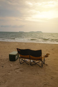 Empty chairs on beach against sky