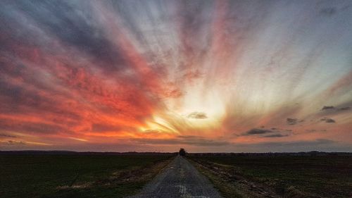 Road amidst field against sky during sunset