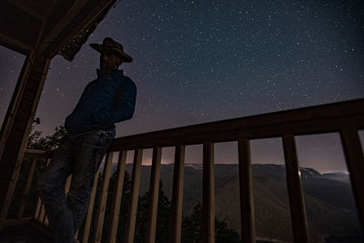 Low angle view of man standing on railing against sky at night
