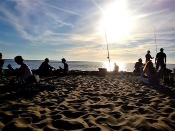 Silhouette people sitting on beach against sky