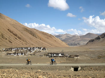 People riding bicycle on sand against sky