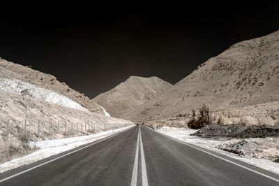 Empty road by mountains against clear sky