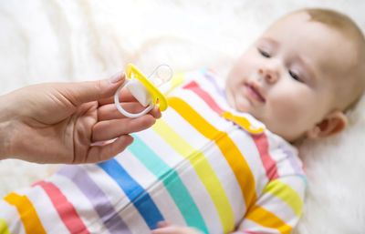 Mother holding pacifier while baby lying on bed
