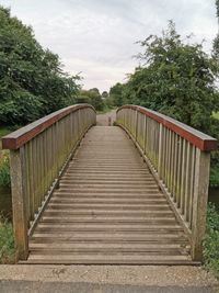 Wooden footbridge along plants and trees against sky