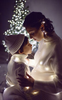 Mother and son in white knitted jumpers holding a garland. background of the tree on christmas