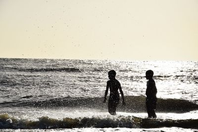 Silhouette people on beach against clear sky