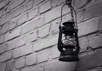 Low angle view of electric lamp hanging against brick wall