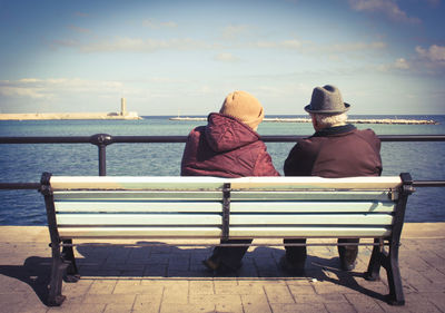 Rear view of women sitting by sea against sky