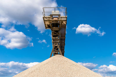 Conveyor over heaps of gravel on blue sky at an industrial cement plant.