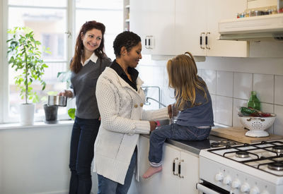 Smiling lesbian couple with girl in kitchen