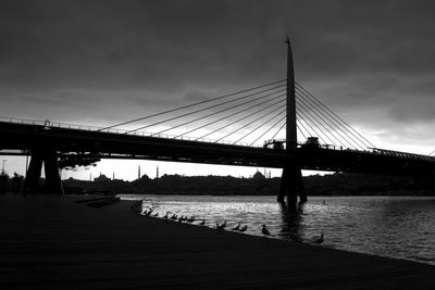 View of suspension bridge over river against cloudy sky