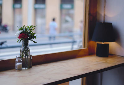 Red flower in glass bottle against window at home