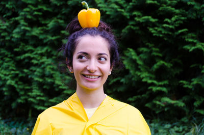 Close-up of smiling young woman with yellow bell pepper on head