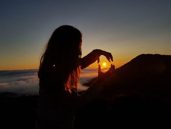 Woman standing against orange sky during sunset