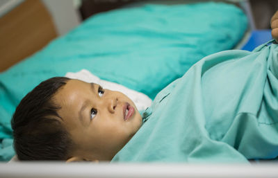 High angle view of cute boy looking away while lying on bed in hospital