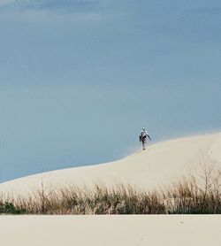 Man walking on sand dune against clear sky