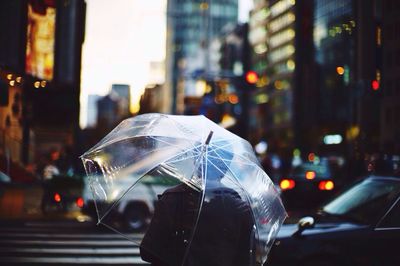 Rear view of man with umbrella walking on street against blurred buildings