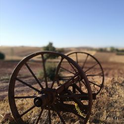 Close-up of rusty wheel on field against clear sky