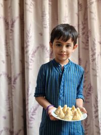 Portrait of smiling boy standing against curtain