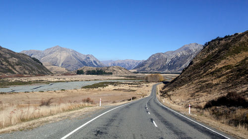 Road leading towards mountains against clear sky