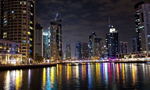 Illuminated buildings by river against sky in city at night