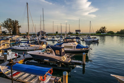 Sailboats moored at harbor against sky during sunset