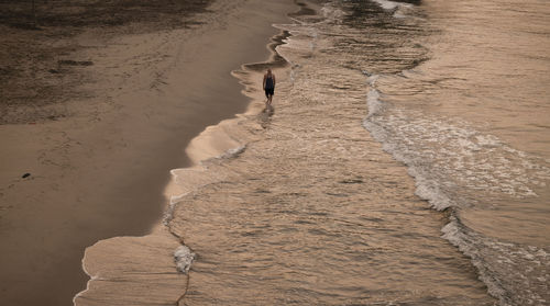 High angle view of adult man walking on beach during sunrise