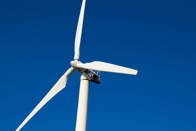 Low angle view of wind turbine against clear blue sky