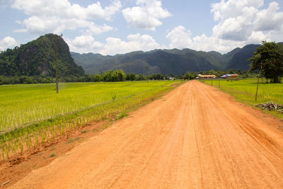 Empty road amidst agricultural field against sky