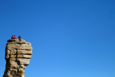 Low angle view of people on rock against clear blue sky