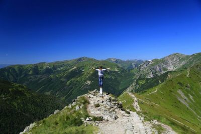 Rear view of man standing on mountain against blue sky